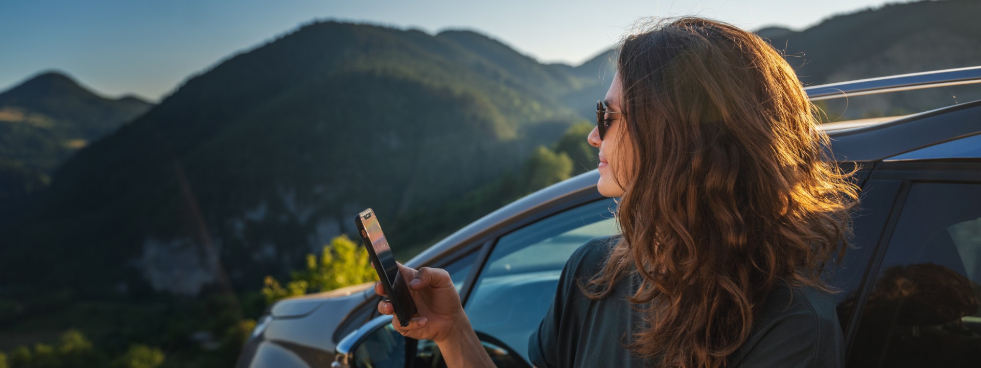 woman holding mobile next to a car