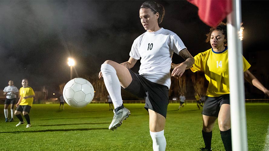 Dzsenifer Marozsán kicking a football in a game as another football player runs up behind her. 
