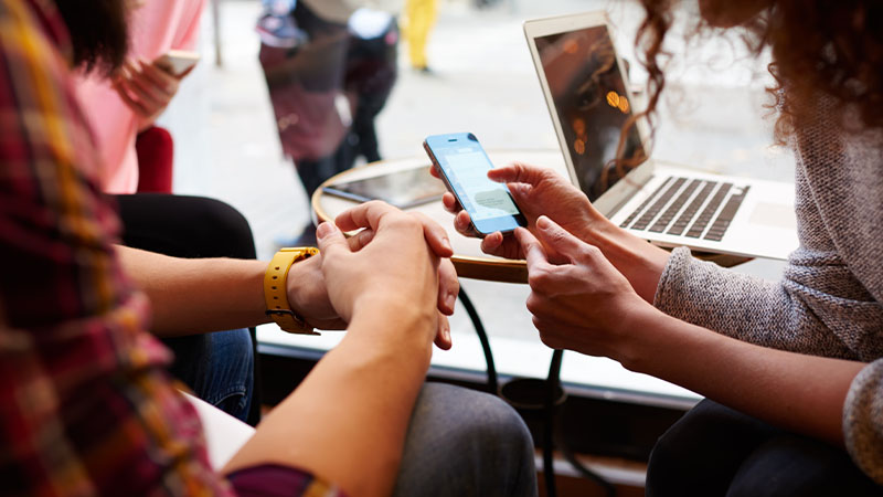 Zwei Personen sitzen im Café und schauen gemeinsam auf ein Smartphone, während sie eine Echtzeitzahlung ausführen.