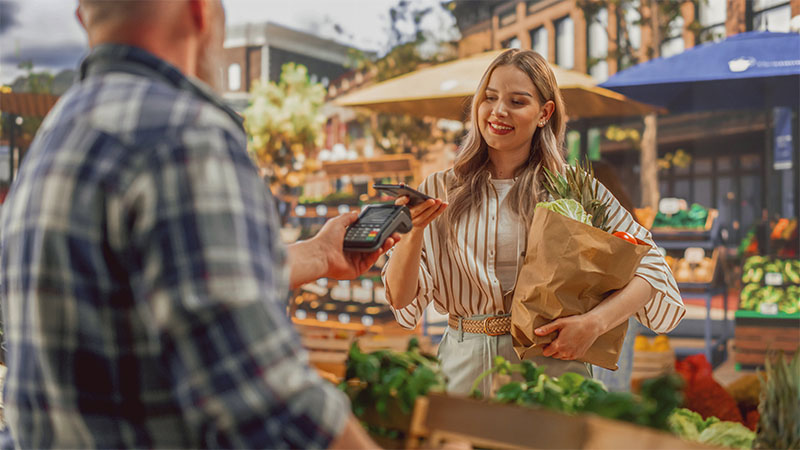 Eine Frau bezahlt auf einem Markt an einem Bezahlterminal mit Visa Karte