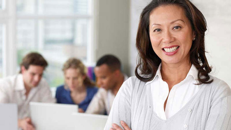 ready-to-return-800x450 Closeup of a woman smiling with three people on their laptops in the background.